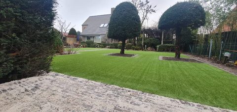 Afgewerkte tuin in Knokke-Heist met kunstgras rond gespaarde bomen, pergola en snoeivormen