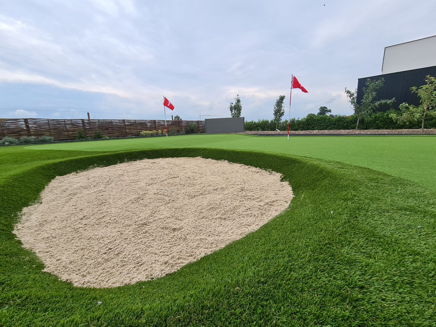 Putting green in kunstgras met twee vlaggen en een zandbunker