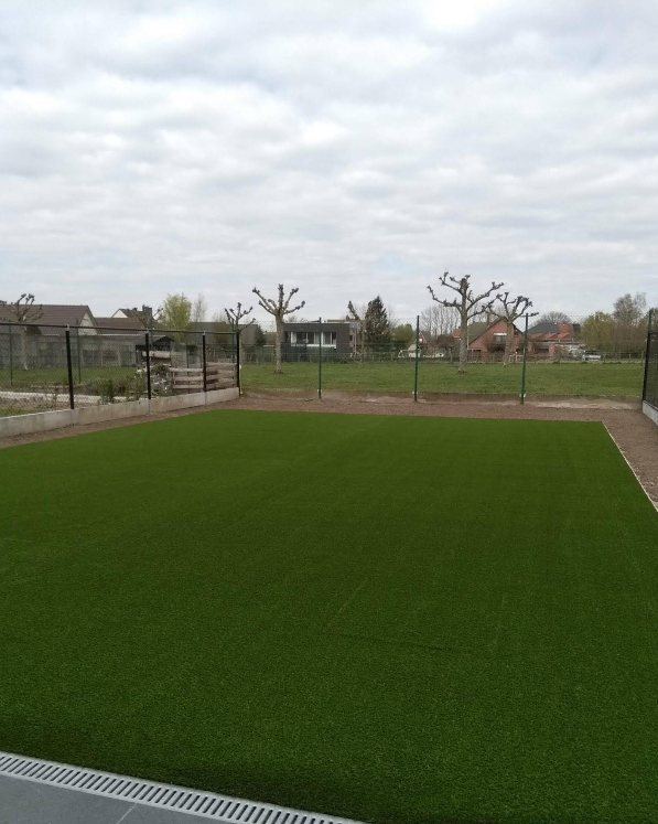 Het kunstgras net gelegd, in het vroege voorjaar met kale bomen